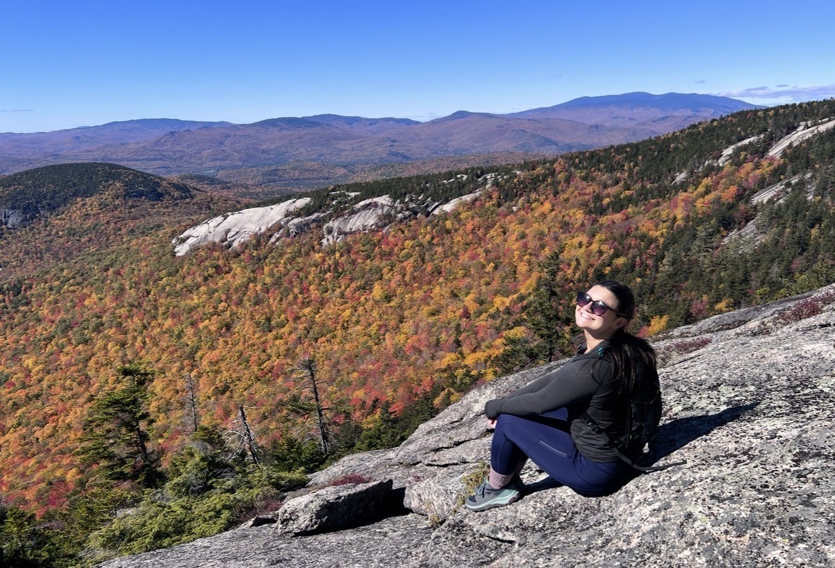 Nicole seated on a rocky overlook above autumn foliage in the White Mountains